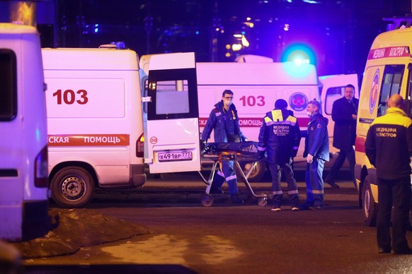 23.03.2024, Russland, Moskau: Sanitäter transportieren eine Leiche zu einem Krankenwagen in der Nähe des brennenden Gebäudes des Crocus City Hall am westlichen Rand von Moskau. Nach dem Angriff auf ei ...