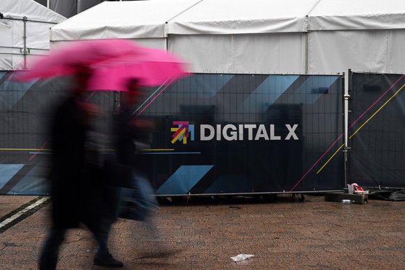 14.09.2022, Nordrhein-Westfalen, Köln: Zwei Männer mit Margenta-Regenschirmen gehen an einem Bauzaun mit der Aufschrift Digital X vorbei. Auf dem Programm der zweitägigen Digital X ging es um die Frag ...