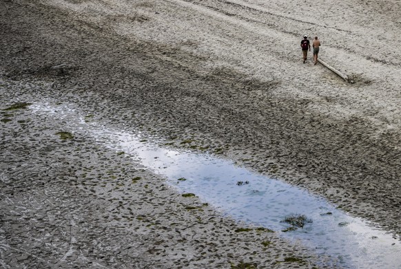 ARCHIV - 11.08.2022, Frankreich, Aiguines: Zwei Männer gehen bei Niedrigwasser über das schlammige Ufer am Stausee Lac de Sainte-Croix. Hitze und ausbleibende Niederschläge sorgten in ganz Frankreich  ...