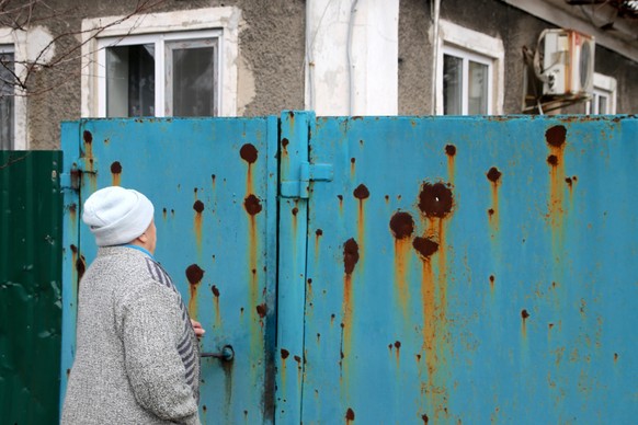 Eine Frau betrachtet einen von Kugeln durchsiebten Zaun in der Stadt Donezk in der Ostukraine.