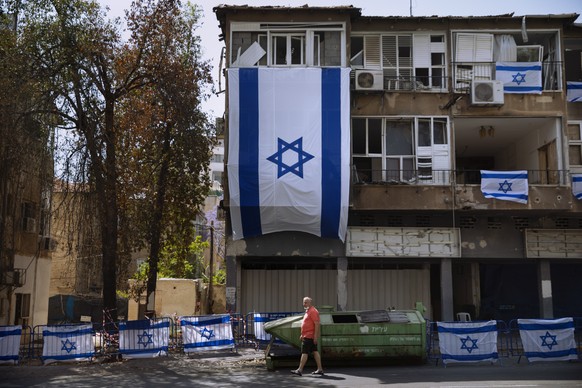 A man walks by a residential building covers with Israeli flags after last week it was hit by a rocket fired from the Gaza Strip, in Ramat Gan, central Israel, Friday, May 21, 2021. A cease-fire took  ...