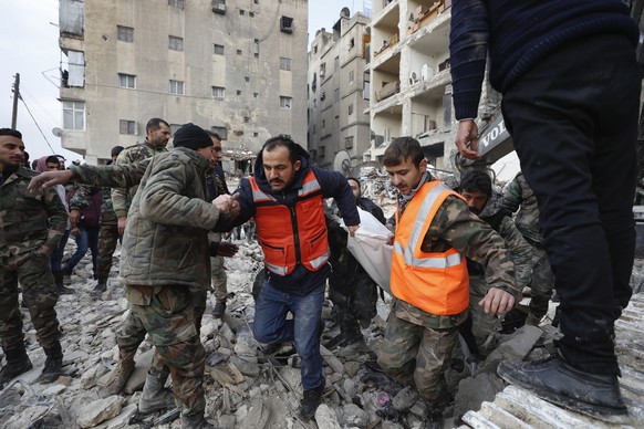 07.02.2023, Syrien, Aleppo: Rettungsteams tragen die Leiche eines Opfers aus einem zerstörten Gebäude. Die Zahl der Toten im Erdbebengebiet an der türkisch-syrischen Grenze steigt - und nach wie vor w ...
