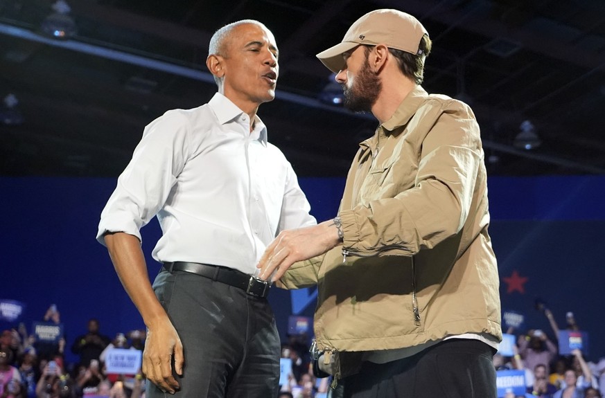 22.10.2024, USA, Detroit: Der Rapper Eminem (r) begrüßt den ehemaligen US-Präsidenten Barack Obama auf der Bühne bei einer Wahlkampfveranstaltung zur Unterstützung der demokratischen US-Präsidentschaf ...