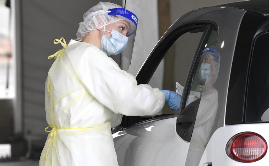 08.10.2020, Finnland, Helsinki: Eine Mitarbeiterin des Gesundheitswesen arbeitet in einer Drive-Thru-Station am Flughafen Helsinki, wo bei dem Fahrer eines Autos einen Abstrich zur Durchf