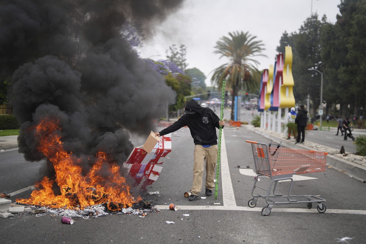A protester places debris in a fire as Border Patrol personnel in riot gear and gas masks stand guard outside an industrial park in Paramount, Calif., on Saturday, June 7, 2025. (AP Photo/Eric Thayer)