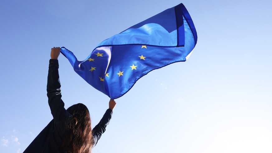 Woman holding European Union flag against blue sky outdoors, low angle view Model Released Property Released xkwx angle back background blue brussels campaign clear cloth color community concept coope ...