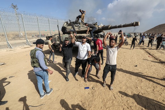 07.10.2023, Palästinensische Gebiete, Khan Yunis: Palästinenser übernehmen die Kontrolle über einen israelischen Panzer, nachdem sie den Grenzzaun zu Israel in Khan Yunis überquert haben. Militante Pa ...