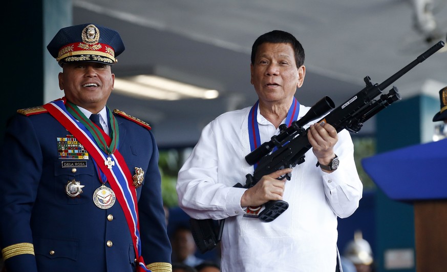 FILE - In this April 19, 2018 file photo, Philippine President Rodrigo Duterte, right, jokes to photographers as he holds an Israeli-made Galil rifle which was presented to him by former Philippine Na ...