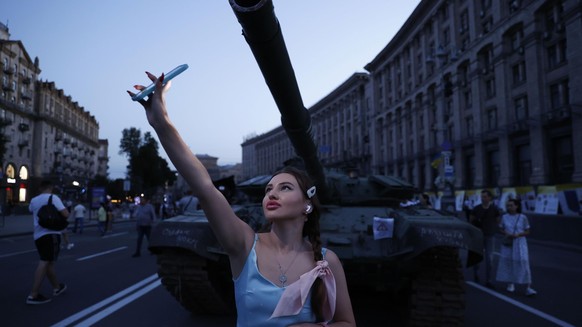 24.08.2022, Ukraine, Kiew: Eine Frau macht ein Selfie vor einem russischen Panzer zwischen zerst