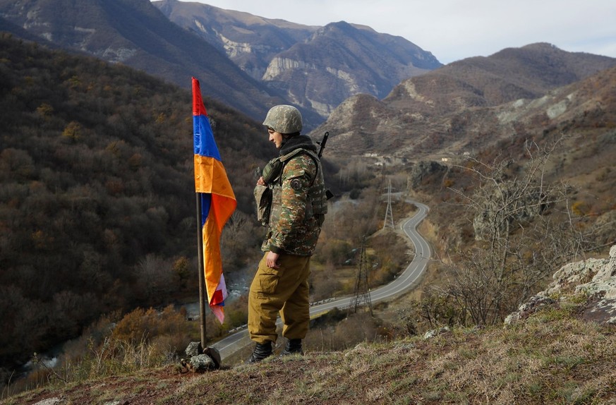 ARCHIV - 25.11.2020, Aserbaidschan, Charektar: Ein armenischer Soldat steht neben der Flagge von Berg-Karabach auf einem Hügel in der Nähe von Charektar in der separatistischen Region Berg-Karabach an ...