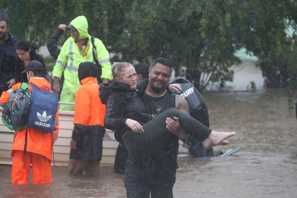 28.02.2022, Australien, Lismore: Ein Mann tr�gt eine Frau durch das Hochwasser einer �berschwemmten Stra�e, w�hrend Rettungskr�ft dahinter weiteren Menschen helfen. Sintflutartiger Regen hat die schwe ...