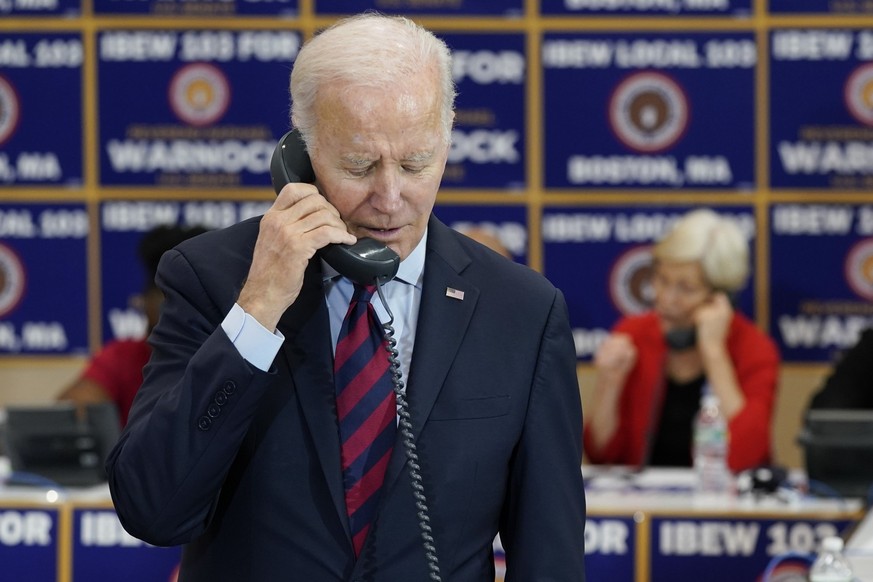 President Joe Biden speaks on the phone while visiting a phone bank at International Brotherhood of Electrical Workers Local 103, Friday, Dec. 2, 2022, in Boston. Sen. Elizabeth Warren, D-Mass., speak ...