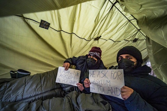 November 26, 2021, Orla, Podlaskie, Poland: Two syrian refugees under a plastic cover in the forests of Poland, ask for asylum with a paper. These refugees crossed illegally the border of Poland from ...