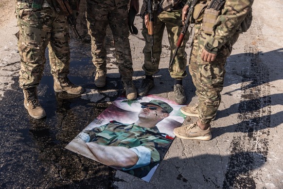 dpatopbilder - 29.11.2024, Syrien, Kafr Naya: Bewaffnete syrische Oppositionskämpfer stellen ihre Füße auf ein Plakat mit einem Foto des syrischen Präsidenten Baschar al-Assad, nachdem sie die Stadt K ...