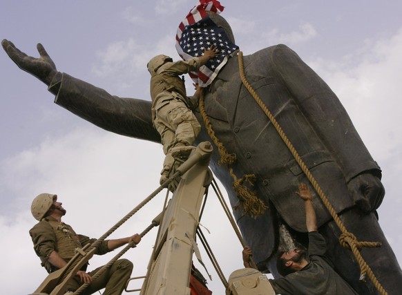 Im April 2003 verdecken in Bagdad US-Marines das Gesicht von Saddam Hussein mit einer amerikanischen Flagge, bevor sie die Statue umstürzen.