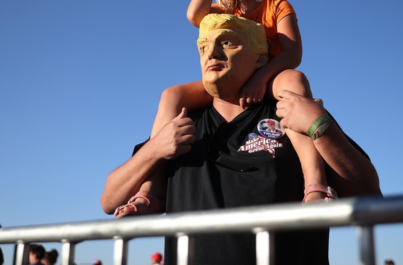 GOODYEAR, ARIZONA - OCTOBER 28: Jason Ingram of Glenville, Arizona, wears a Donald Trump mask with his daughter Leanna, 5, on his shoulders at the conclusion of a campaign rally with the president at  ...
