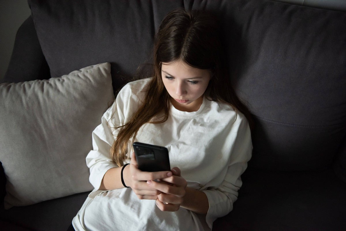 Ein trauriges Teenager-Mädchen liegt mit einem Smartphone in der Dunkelheit. Traurigkeit, Probleme. Das Konzept der Kurzsichtigkeit. A sad teenage girl is lying with a smartphone in the dark. Sadness, ...
