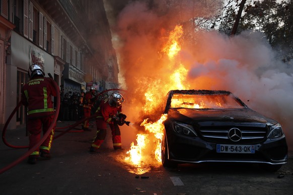 28.11.2020, Frankreich, Paris: Feuerwehrkräfte löschen ein Feuer in einem brennenden Auto während einer Demonstration gegen ein umstrittenes Sicherheitsgesetz. Mehr als Hunderttausend Menschen sind in ...