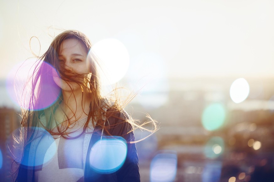 Young Woman Standing in Sunset Light, Looking at Camera. Hair Fluttering in the Windi. Selective Focus, Bokeh Lights.

511729200