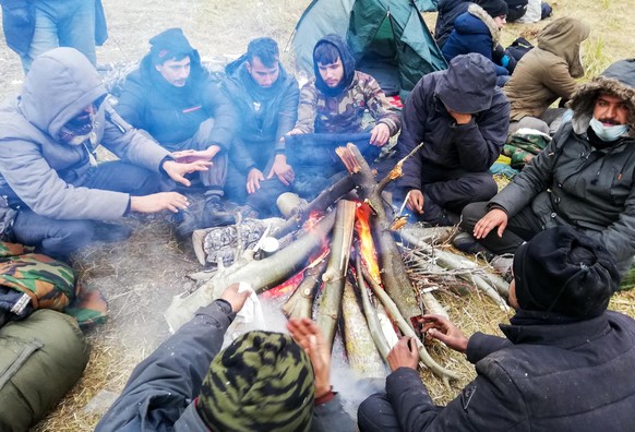 GRODNO REGION, BELARUS - NOVEMBER 16, 2021: Migrants sit by a bonfire at the Bruzgi - Kuznica crossing point on the Belarusian-Polish border. The migrant crisis on the border of Belarus with Poland, L ...