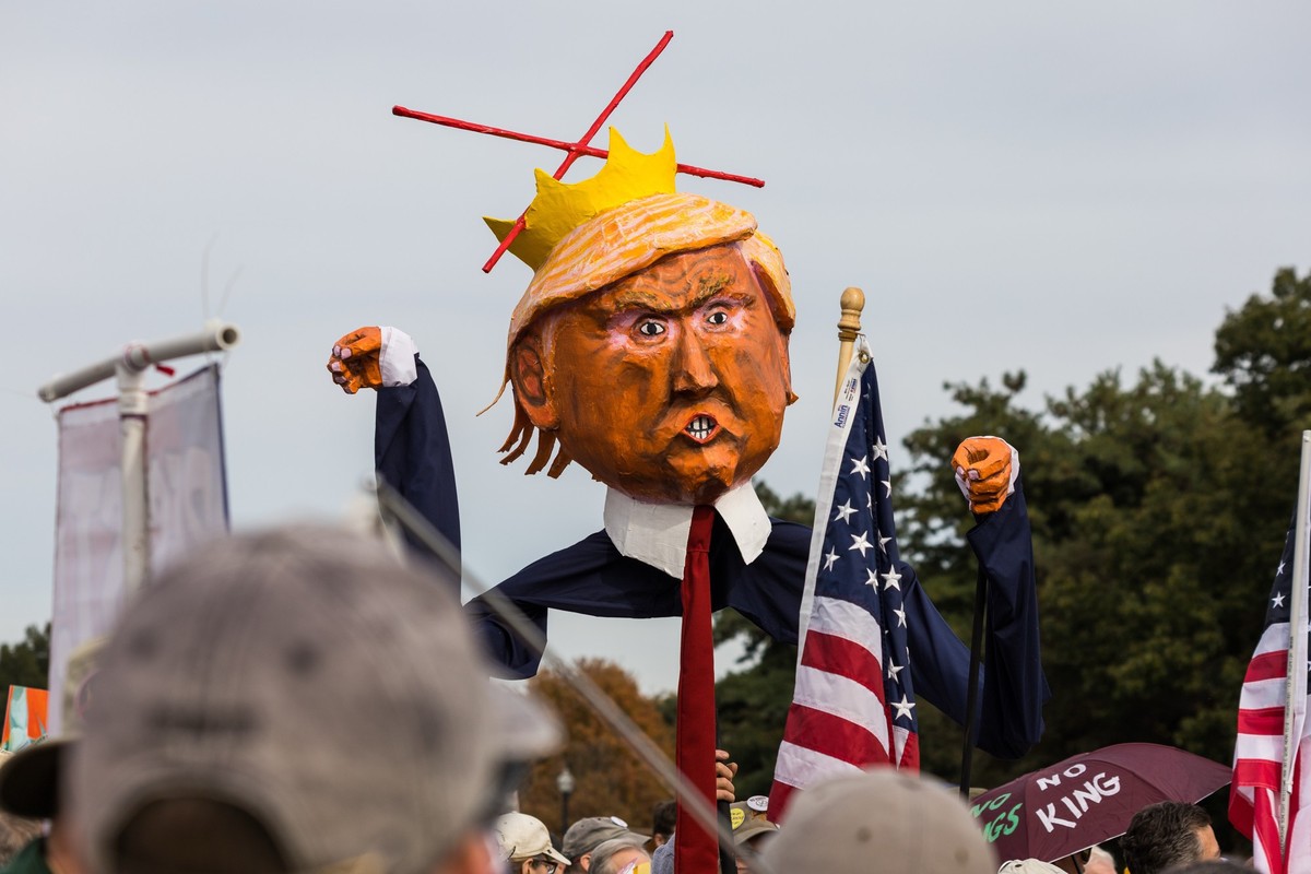18.10.2025, USA, Washington: Demonstranten halten ein Bildnis von US-Präsident Trump in der Nähe des Arlington Nationalfriedhofs, während sie sich darauf vorbereiten, im Rahmen der &quot;No Kings Day- ...