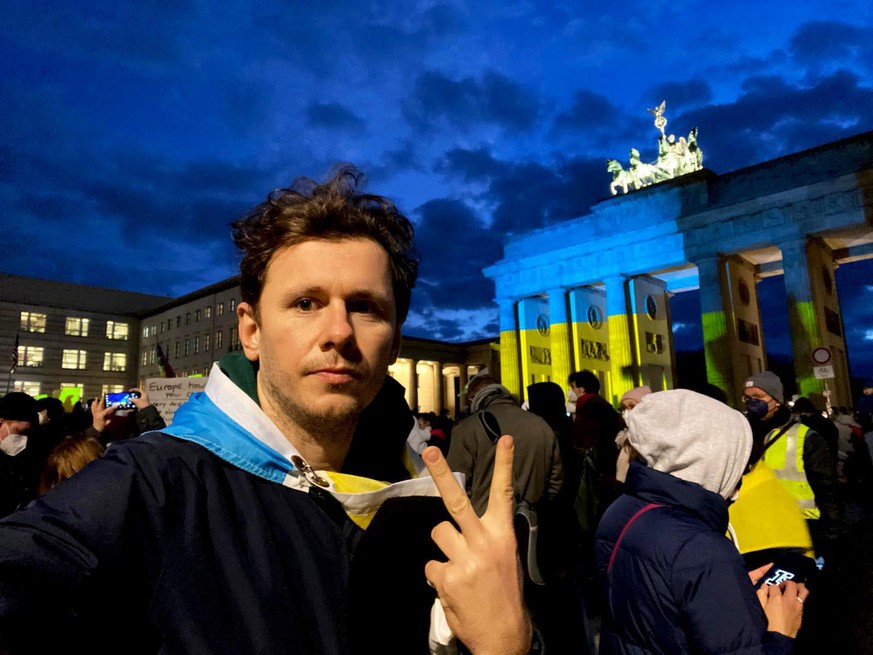 Dimitri auf einer Friedensdemo in Berlin. Das Brandenburger Tor wird in den ukrainischen Nationalfarben beldeuchtet.