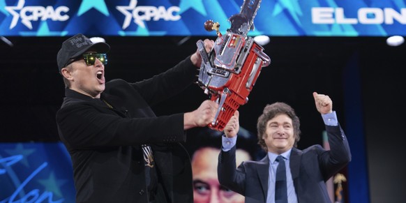 20.02.2025, USA, Oxon Hill: Elon Musk hält eine Kettensäge hoch, die er vom argentinischen Präsidenten Javier Milei (r) erhalten hat, als sie auf der Conservative Political Action Conference (CPAC) im ...