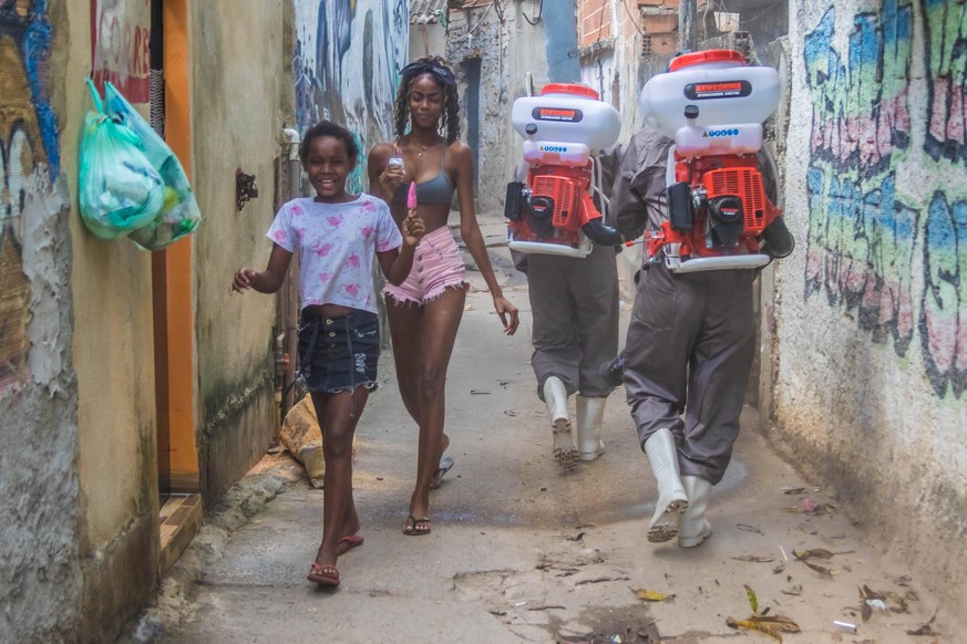 Das Virus der Reichen trifft längst auch die Armen: In einem Slum im Norden von Rio begegnen zwei Mädchen zwei Personen, die dort desinfizieren.