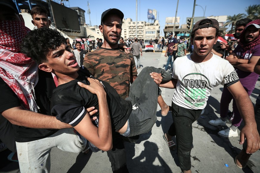 ARCHIV - 01.10.2022, Irak, Bagdad: Regierungsgegner tragen einen Verletzten nach Zusammenstößen während einer Demonstration anlässlich des dritten Jahrestages der Anti-Regierungs-Proteste auf dem Tahr ...