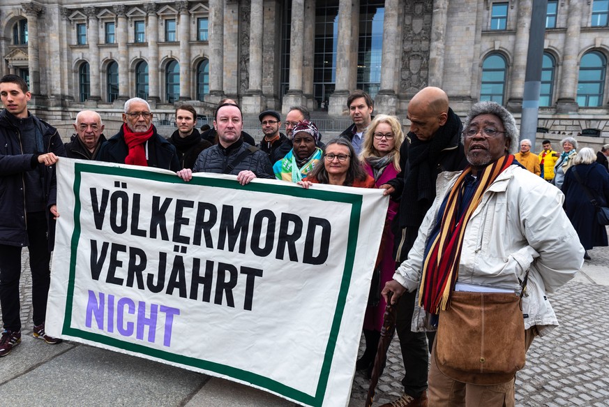 V??lkermord verj??hrt nicht steht auf dem Transparent von Aktivisten waehrend der Protestaktion zum V??lkermord an den Herero und Nama am 21.03.2019 vor dem Bundestag in Berlin, Deutschland. Am Weltta ...