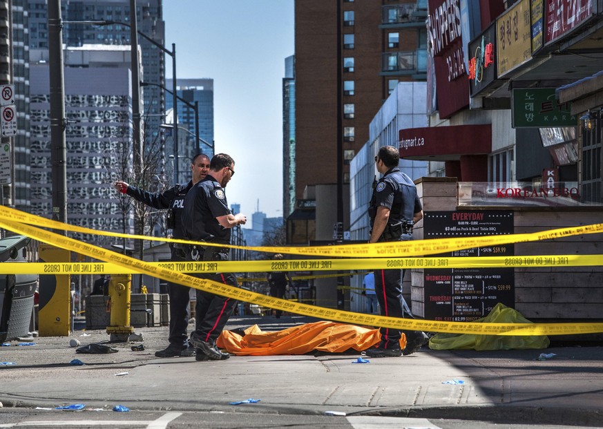 Police officers stand by a body covered on the sidewalk in Toronto after a van mounted a sidewalk crashing into a crowd of pedestrians on Monday, April 23, 2018. The van apparently jumped a curb Monda ...