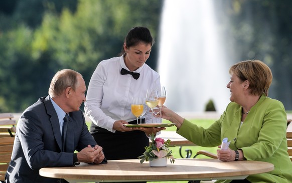 German Chancellor Angela Merkel, right, and Russian President Vladimir Putin are delivered drinks as they talk during their meeting at the government guest house Meseberg in Gransee near Berlin, Germa ...