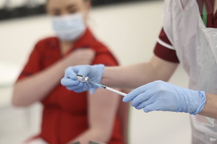 A nurse prepares a COVID-19 vaccine before administering it to Sister Joanna Sloan, left, the first person in Northern Ireland to receive the Pfizer-BioNTech COVID-19 vaccine at the Royal Victoria Hos ...