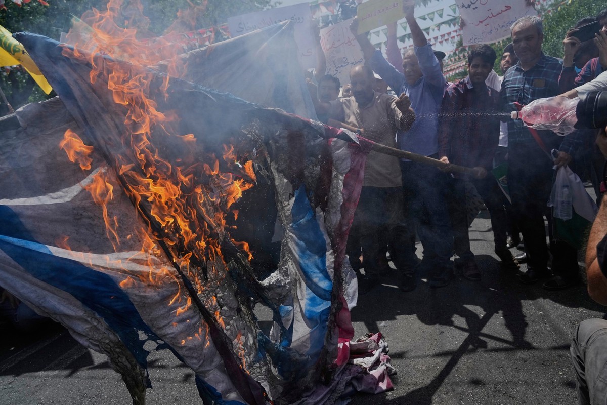 20.06.2025, Iran, Teheran: Iranische Demonstranten verbrennen eine israelische und eine US-amerikanische Flagge während einer Demonstration zur Verurteilung israelischer Angriffe auf mehrere Städte im ...