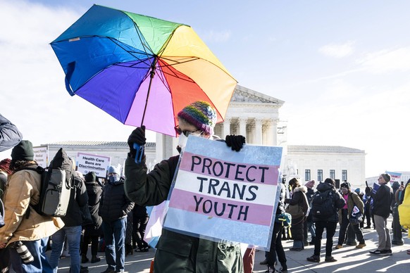 December 4, 2024, Washington, District Of Columbia, USA: A person holding a rainbow umbrella and a sign saying Protect trans youth at a demonstration against a Tennessee law banning puberty blockers a ...