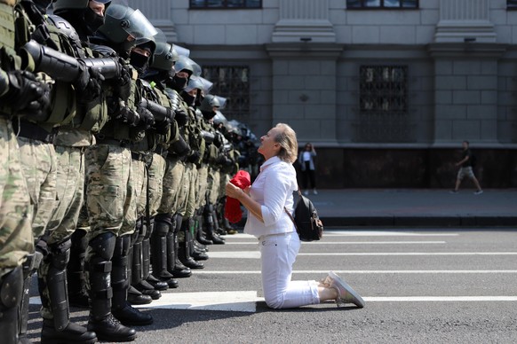 Eine Frau kniet vor belarussischen Sicherheitsbeamten.