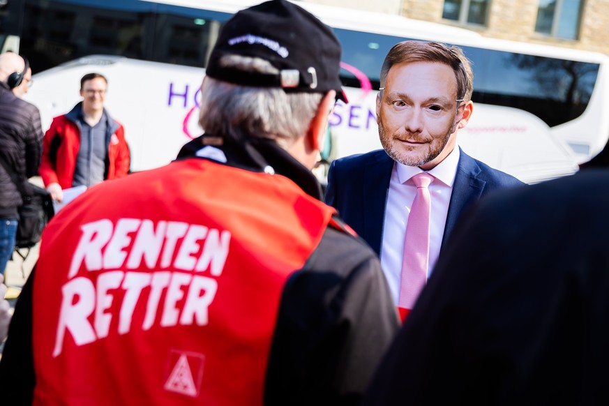 21.04.2023, Berlin: Eine Person trägt vor dem Veranstaltungsort des FDP-Bundesparteitags bei einem Protest der IG Metall gegen die Aktienrente eine Maske des FDP-Bundesvorsitzenden Lindner. Auf der Ta ...
