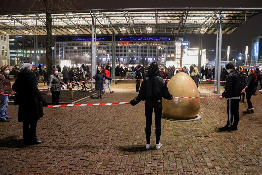 Demonstranten gegen die Anti-Corona-Proteste halten ein rot-weisses Absperrband um das Denkmal «Demokratieglocke» auf dem Augustusplatz. In der Leipziger Innenstadt finden Demonstrationen unter dem Mo ...