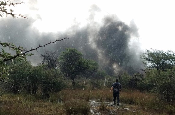 In this Tuesday, July 31, 2018 photo provided by Alberto Herrera, a survivor stands in a rain shower in a field watching smoke billow from the downed Aeromexico jetliner he was traveling in, near the  ...
