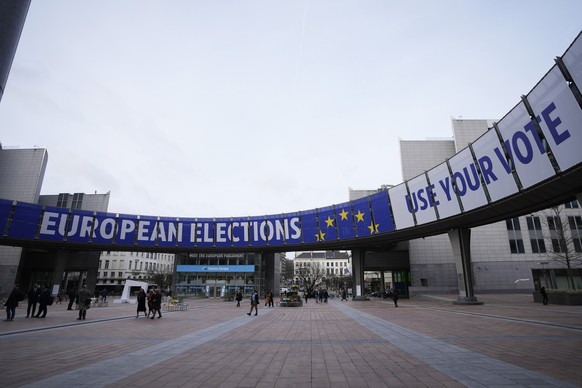 People walk under a banner advertising the European elections outside the European Parliament in Brussels, Wednesday, Jan. 24, 2024. European elections will take place from June 6 to June 9, 2024, in  ...