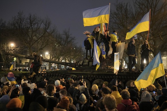 People wave Ukrainian flags as they stand on top of a wreck of a Russian T-72 tank, destroyed on the approach to Kyiv and placed in front of the Russian Embassy during a demonstration to mark the firs ...
