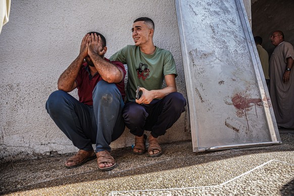 07.10.2023, Palästinensische Gebiete, Gaza: Zwei Männer trauern neben den Kühlräumen einer Leichenhalle. Die im Gazastreifen herrschende islamistische Hamas, die von Israel, der EU und den USA als Ter ...
