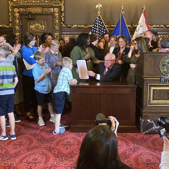 Democratic Minnesota Gov. Tim Walz jokes with kids as he shows off a bill he signed at the State Capitol in St. Paul, Minn., on Thursday, May 25, 2023, to establish a paid family and medical leave pro ...