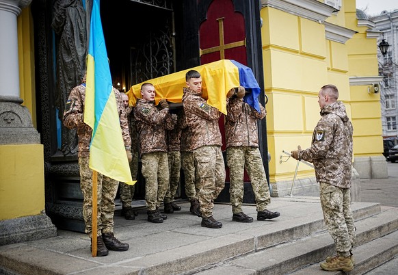 24.02.2023, Ukraine, Kiew: Kameraden des gefallenen Soldaten Jurij Strojew tragen nach einer Trauerfeier den Sarg aus der Wladimirkathedrale. Der 51-jährige Vater von zwei Kindern wurde am 17. Februar ...