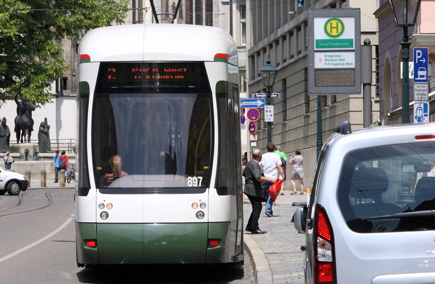 Eine Straßenbahn hält in Augsburg an einer Haltestelle nahe des Doms.