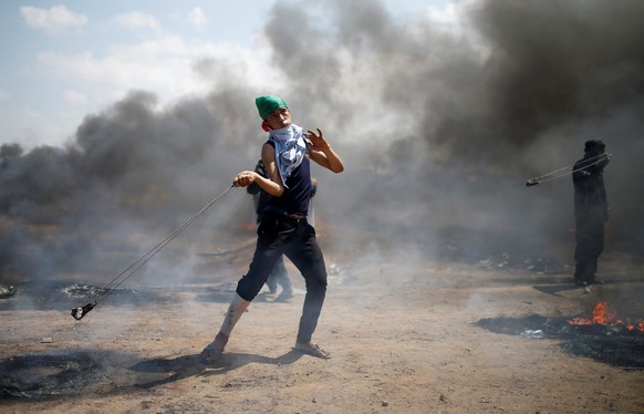 A Palestinian demonstrator uses a sling to hurl stones at Israeli troops during a protest against U.S. embassy move to Jerusalem and ahead of the 70th anniversary of Nakba, at the Israel-Gaza border e ...