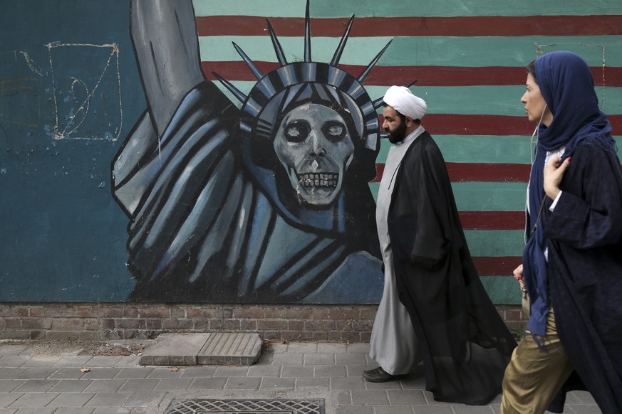 A cleric and a woman walk past an anti-U.S. mural painted on the wall of the former U.S. Embassy in Tehran, Iran, Tuesday, May. 8, 2018. President Donald Trump prepared to tell the world Tuesday wheth ...