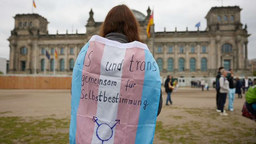 12.04.2024, Berlin: Eine Teilnehmerin steht bei einer Protestveranstaltung gegen das Selbstbestimmungsgesetz von Frauengruppen mit einer Transgender-Pride-Flagge vor dem Bundestag. Die Teilnehmer des  ...