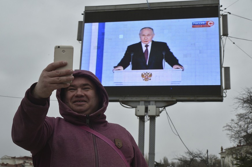 A man makes a selfie in front of a tv screen showing Russian President Vladimir Putin during his annual state of the nation address in in Sevastopol, Crimea, Tuesday, Feb. 21, 2023. (AP Photo)