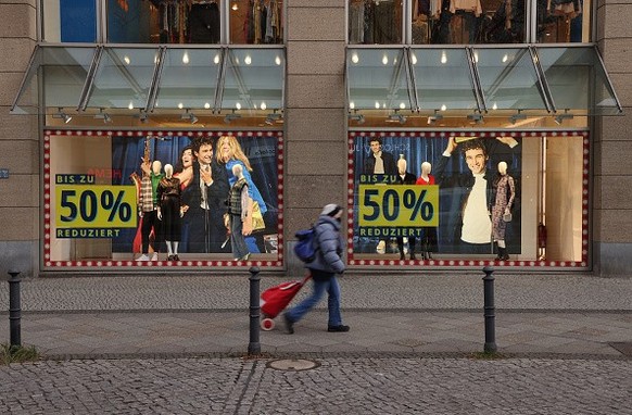 BERLIN, GERMANY - DECEMBER 20: A shopper walks past signs advertising sales at a department store on the main shopping street in Steglitz district during the fourth wave of the novel coronavirus pande ...